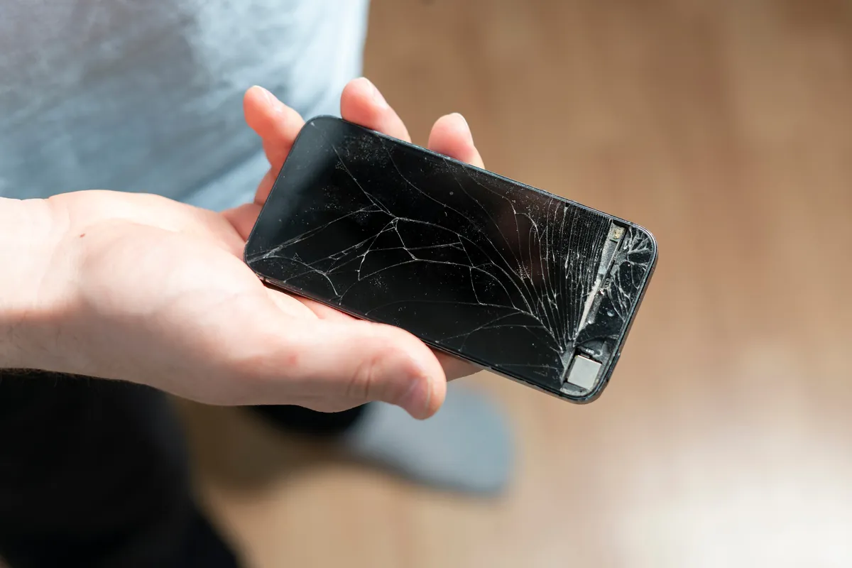 Main tenant un smartphone à l'écran fissuré au-dessus d'une table