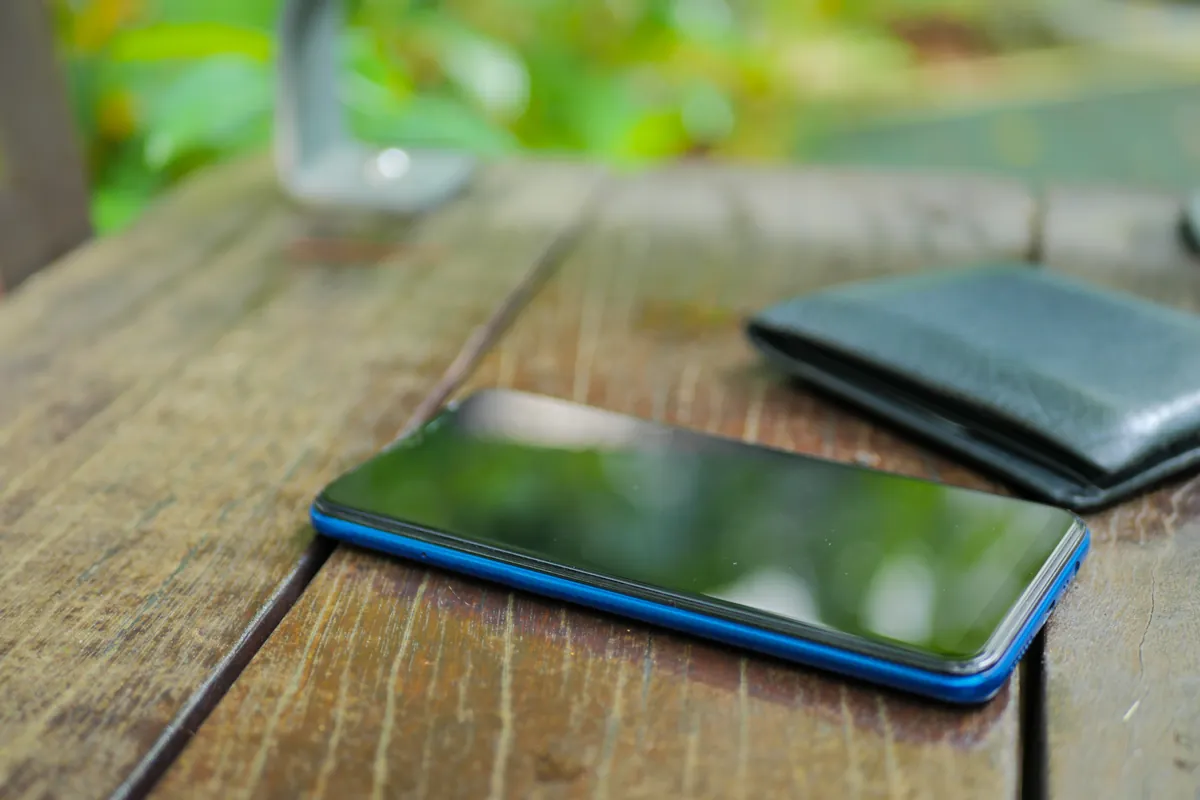 Smartphone à coque bleue posé sur une table en bois à côté d'un portefeuille