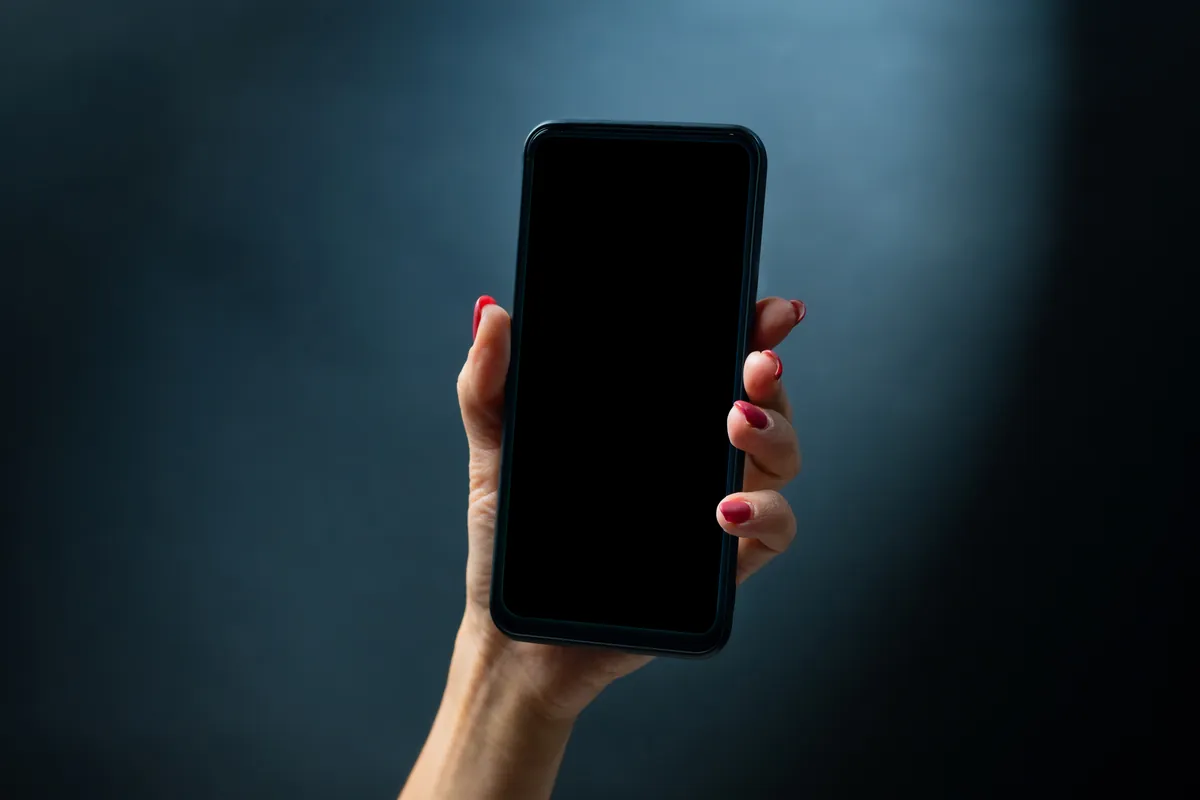 Main tenant un smartphone à l'écran noir sur un fond sombre