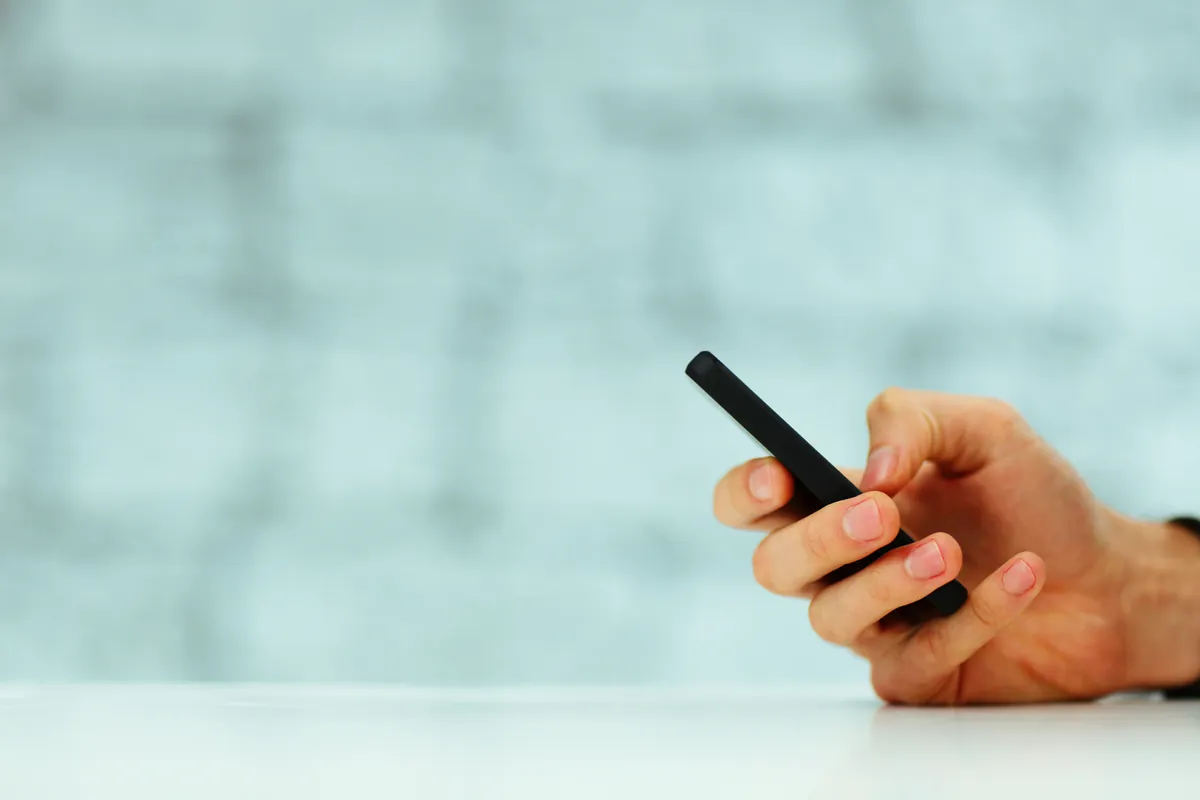 Main tenant un smartphone au-dessus d'une table blanche, recherche d'un numéro de téléphone
