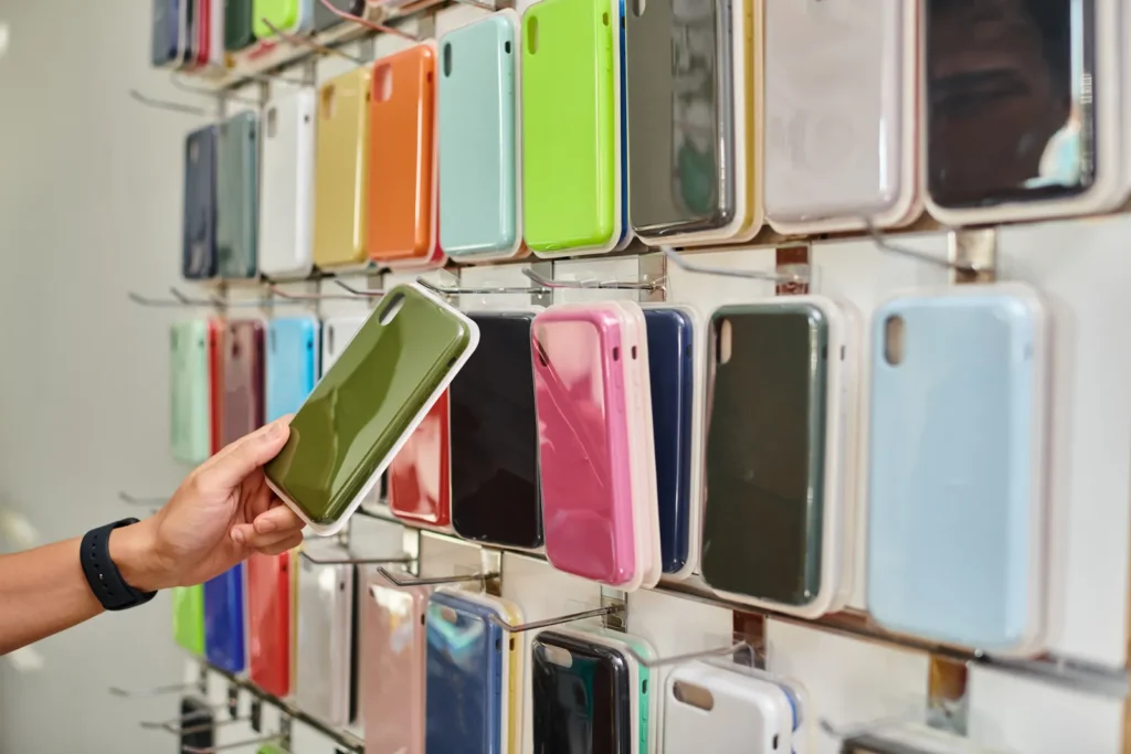Main choisissant une coque de téléphone verte devant un mur de coques colorées en magasin