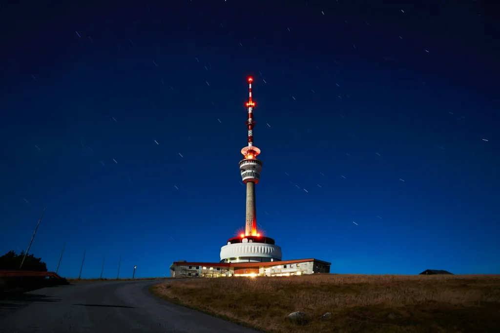 Tour de télécommunication illuminée sur une colline, sous un ciel de nuit bleu étoilé
