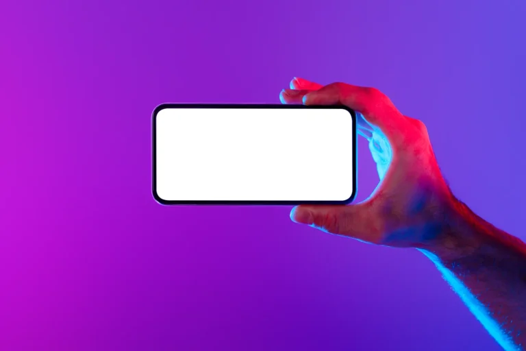 Main éclairée en rose tenant un smartphone à l’écran blanc sur un fond violet