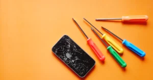 Smartphone à l'écran fissuré et tournevis colorés de réparation sur fond orange