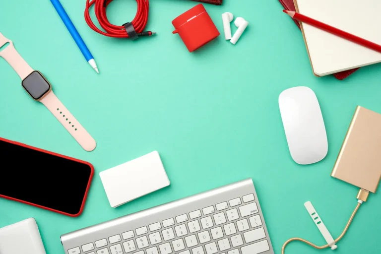 Vue de dessus d’un clavier, d’une souris, d’un smartphone, d’une montre connectée et d’écouteurs sur fond vert d’eau